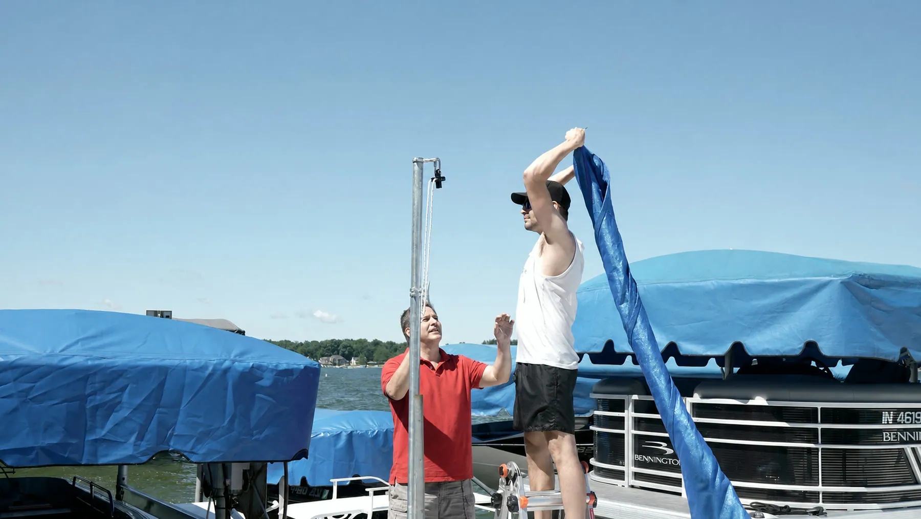 Two DockShade installers raising the blue shade beside its galvanized dock post